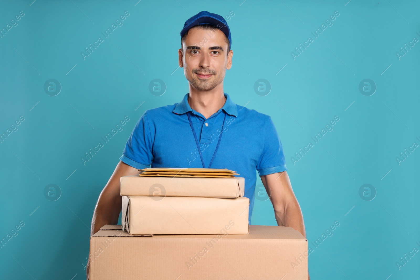 Photo of Happy young courier with parcels and envelopes on blue background