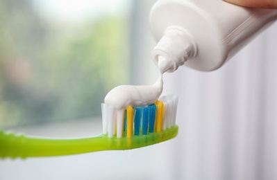 Photo of Applying paste on toothbrush against blurred background, closeup