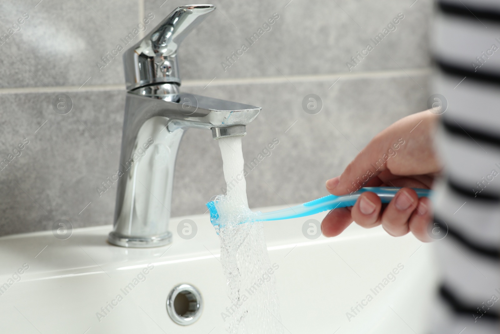 Photo of Woman washing plastic toothbrush under flowing water from faucet in bathroom, closeup