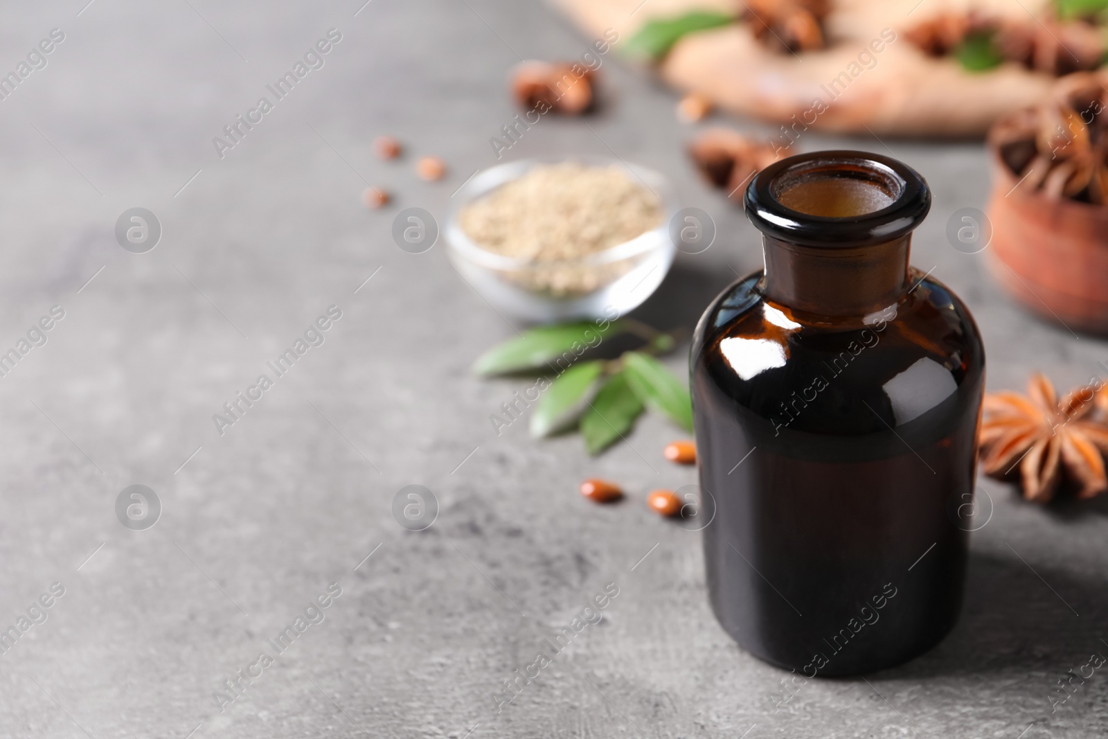 Photo of Bottle of essential oil and anise on grey table. Space for text