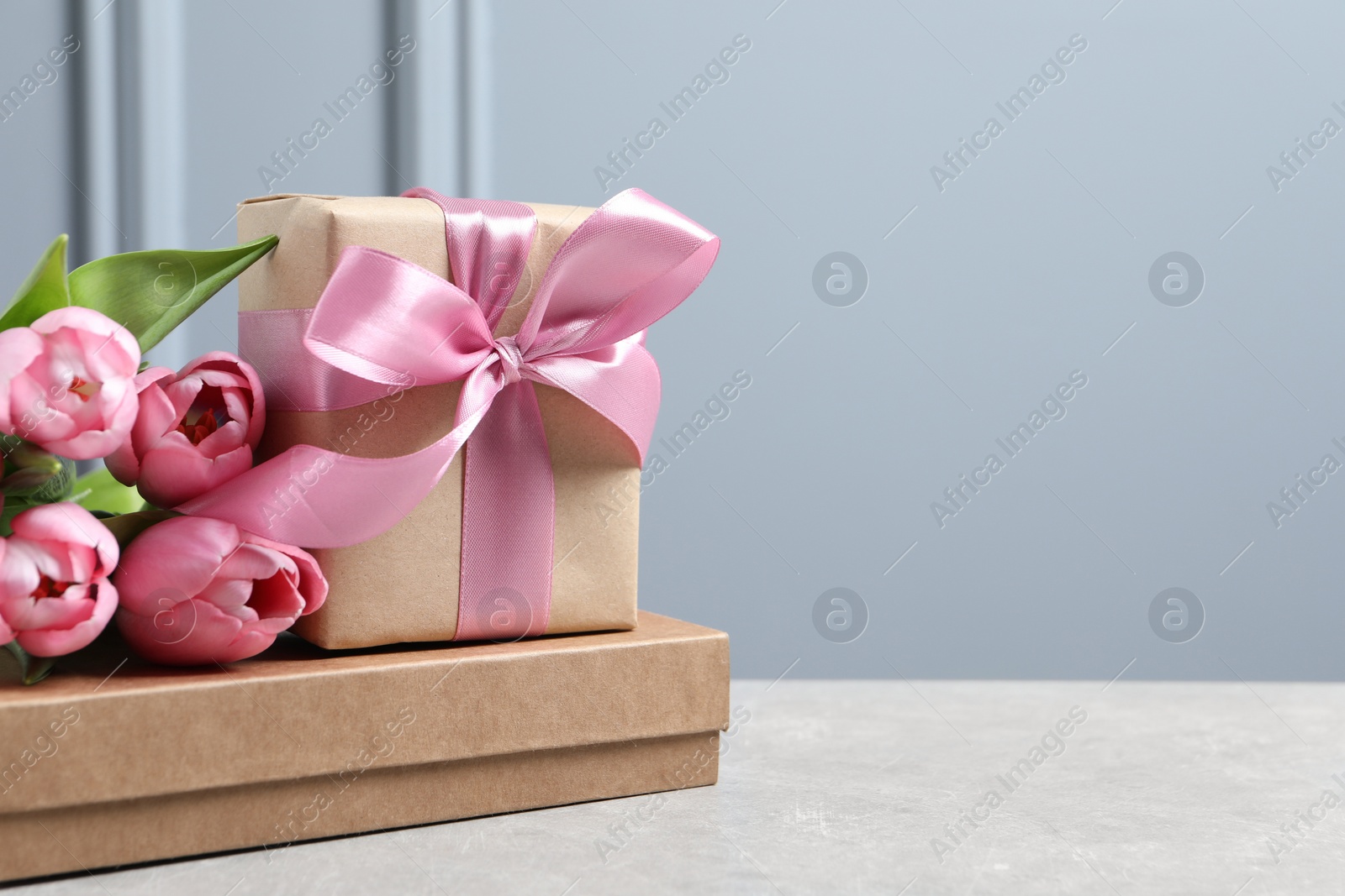 Photo of Beautiful gift box with bow and pink tulip flowers on light table, space for text