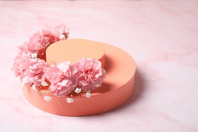 Photo of Orange geometric figures, gypsophila and carnation flowers on pink marble table, closeup with space for text. Stylish presentation for product
