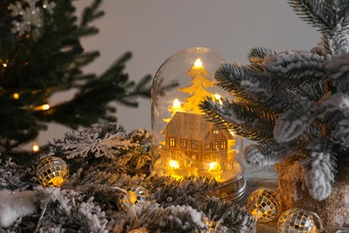 Beautiful snow globe with house model, glowing fairy lights inside and Christmas decor on wooden table