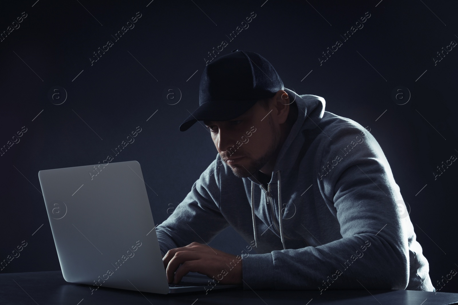 Photo of Man using laptop at table on dark background. Criminal activity