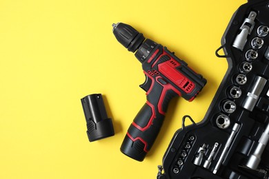 Photo of Electric screwdriver and case with bits on yellow background, flat lay