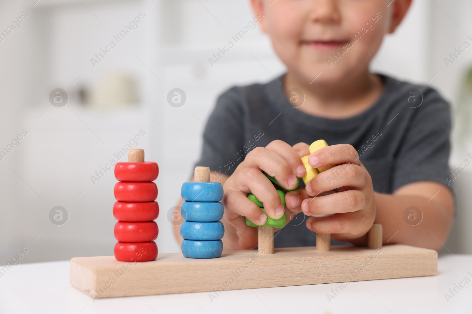 Photo of Motor skills development. Little boy playing with stacking and counting game at table indoors, closeup