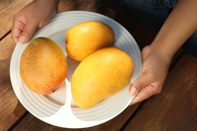 Woman holding plate with tasty mangoes at wooden table, closeup
