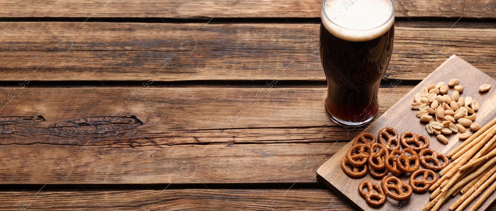 Image of Glass of beer served with delicious pretzel crackers and other snacks on wooden table, space for text. Banner design