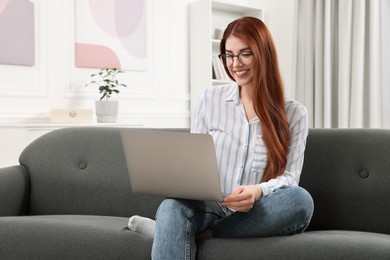 Happy woman using laptop on couch in room