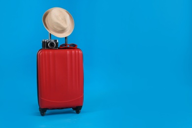 Travel suitcase with hat, camera and sunglasses on light blue background, space for text. Summer vacation