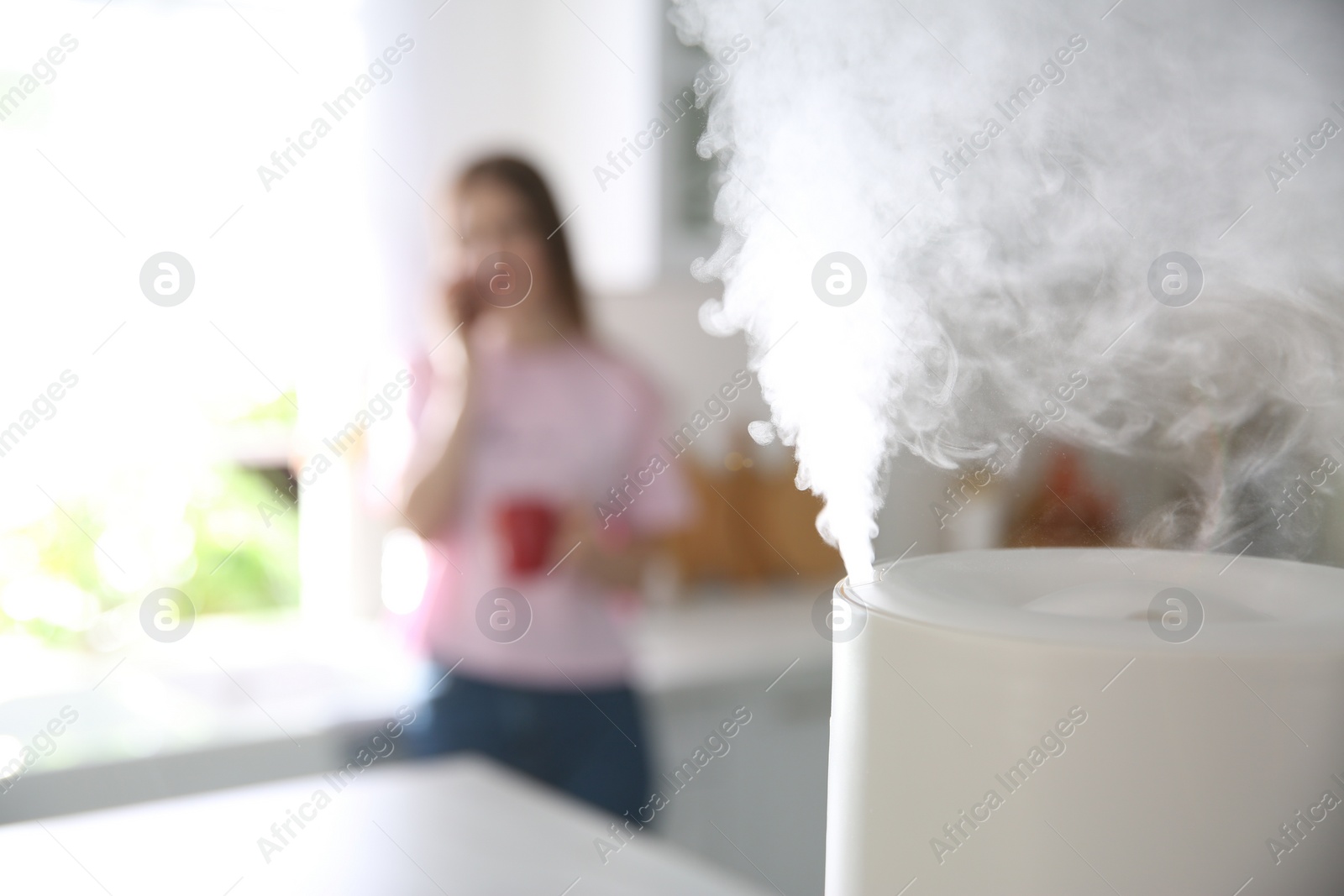 Photo of Modern air humidifier and blurred woman in kitchen