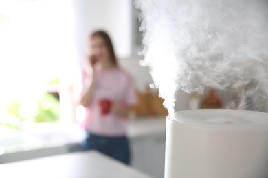 Modern air humidifier and blurred woman in kitchen