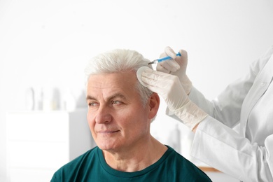 Senior man with hair loss problem receiving injection in salon