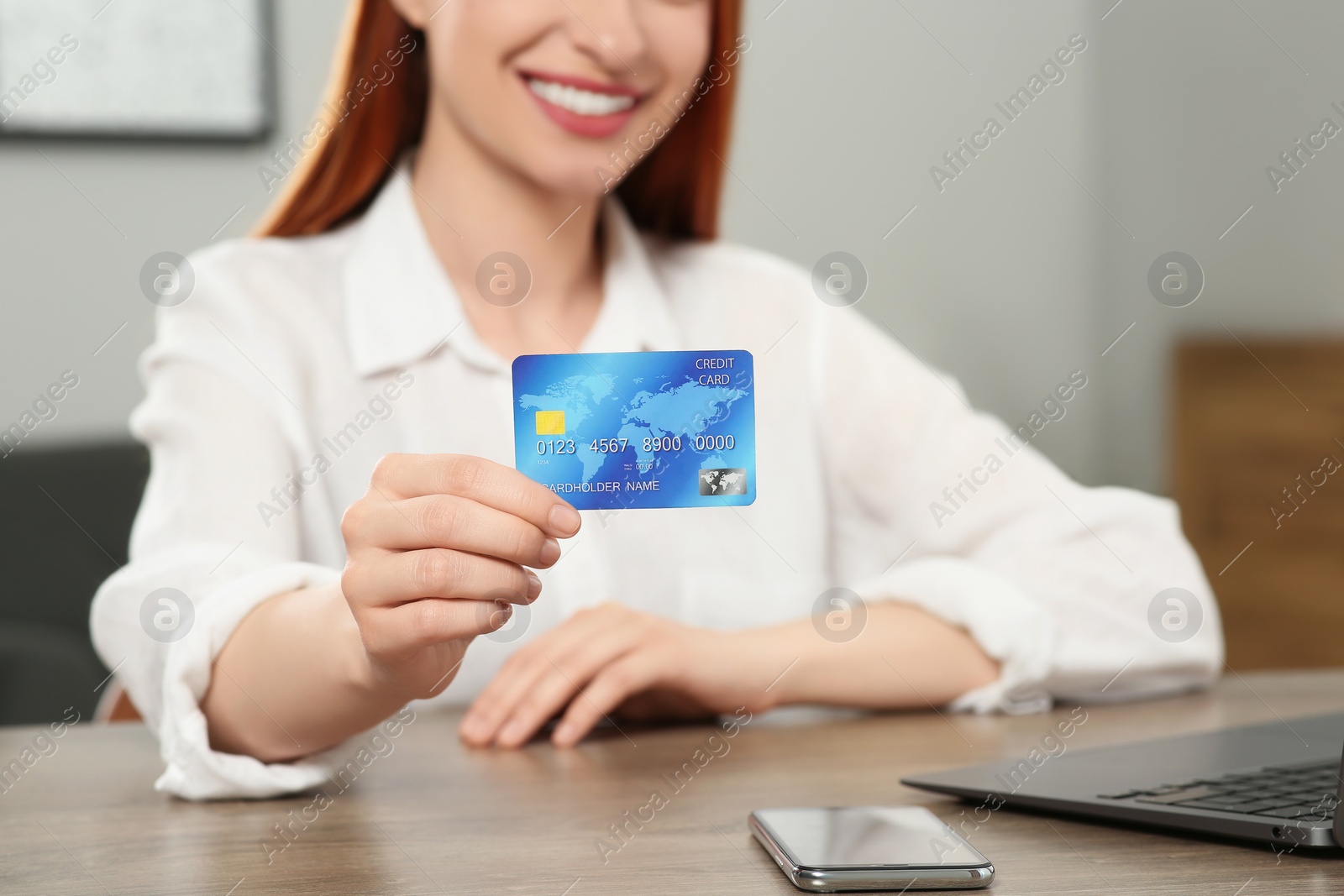 Photo of Woman with credit card near laptop at wooden table indoors, closeup. Online shopping