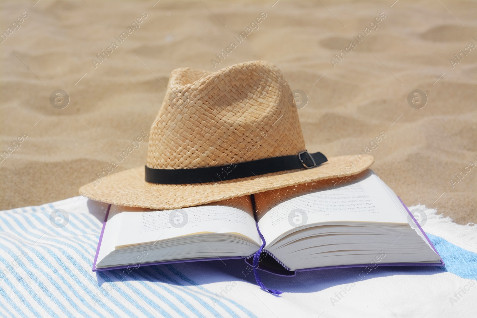 Photo of Beach towel with open book and straw hat on sand
