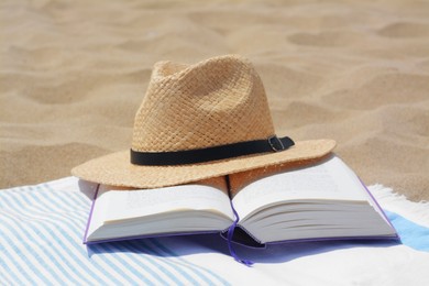 Beach towel with open book and straw hat on sand