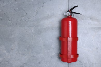 Fire extinguisher on grey wall, space for text