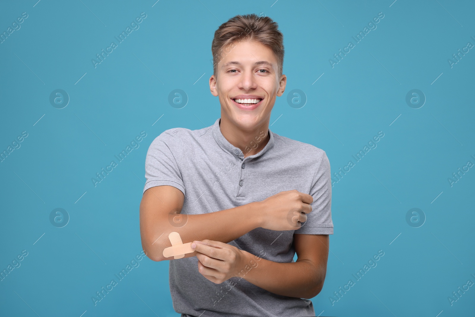 Photo of Handsome man putting sticking plasters onto elbow on light blue background