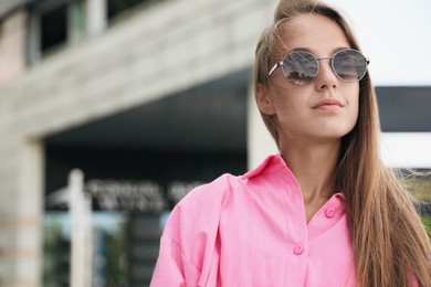 Photo of Beautiful young woman in stylish sunglasses on city street, space for text