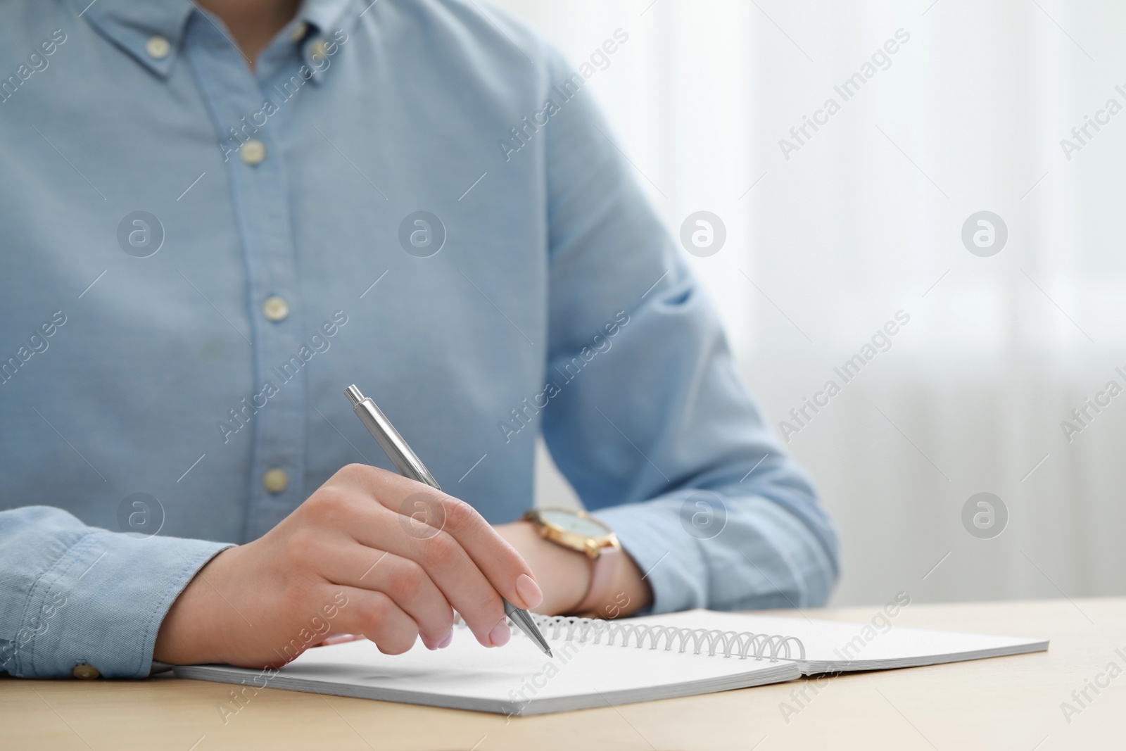 Photo of Woman writing in notebook at wooden table, closeup