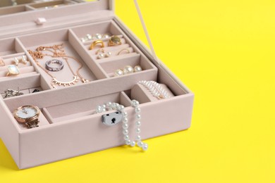 Jewelry box with many different accessories on yellow background, space for text