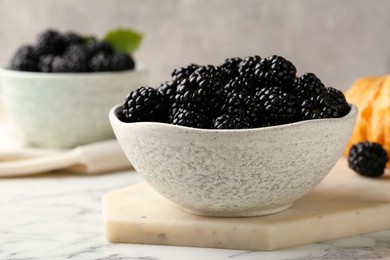 Bowl of fresh ripe blackberries on white marble table, closeup