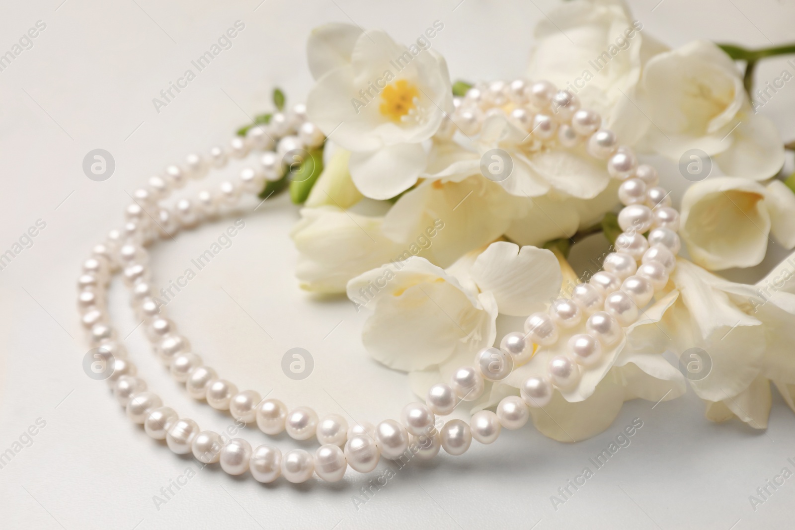 Photo of Beautiful pearl necklace and flowers on white marble table, closeup