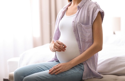 Photo of Young pregnant woman smoking cigarette at home, closeup