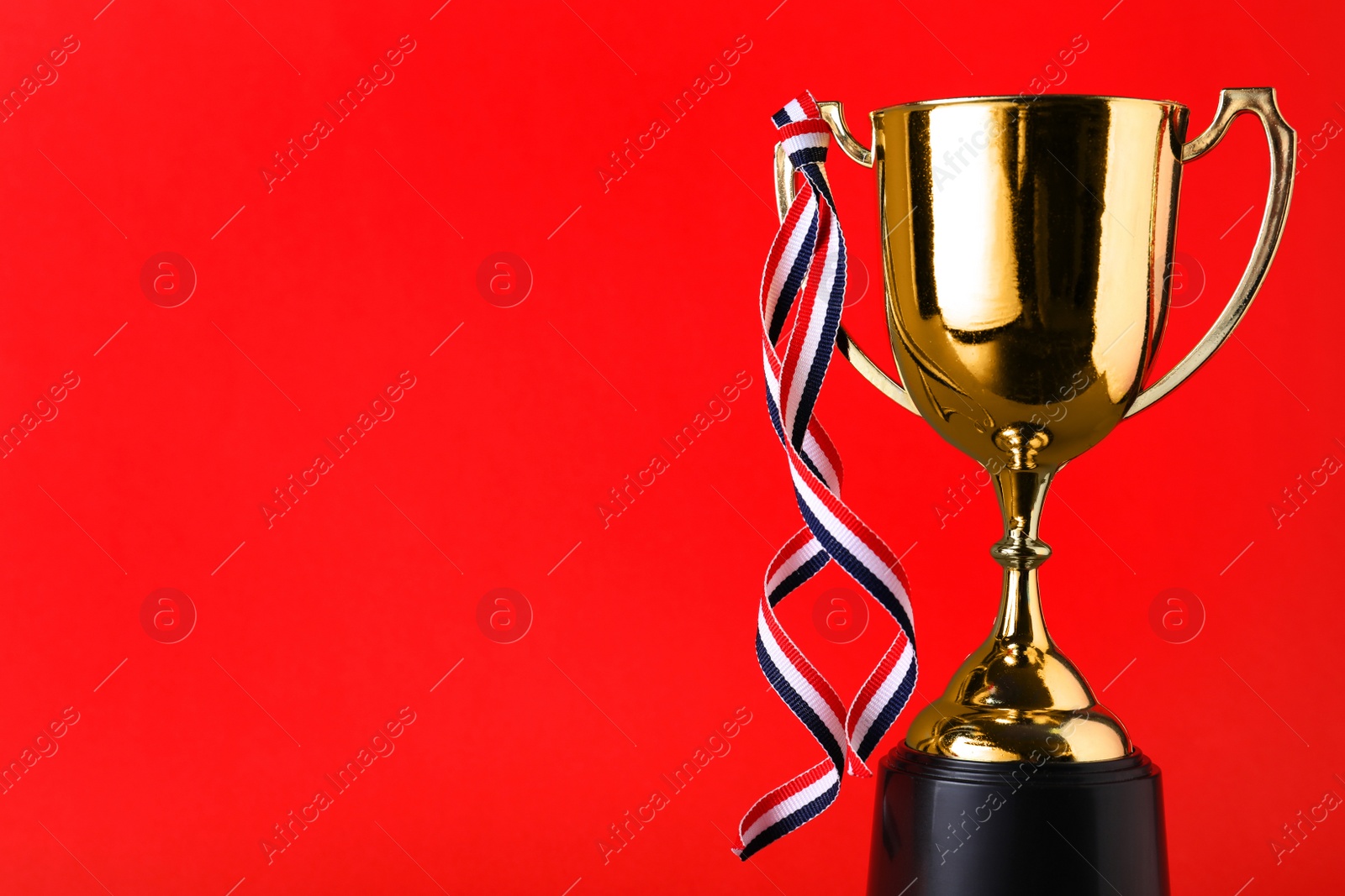 Photo of Golden trophy cup with ribbon on red background. Space for text