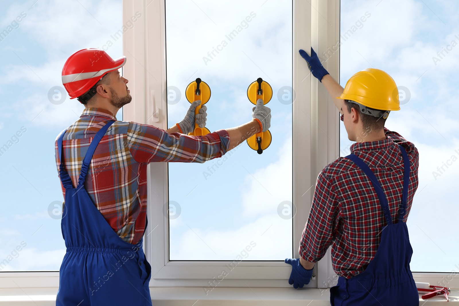 Photo of Workers using suction lifters during plastic window installation indoors