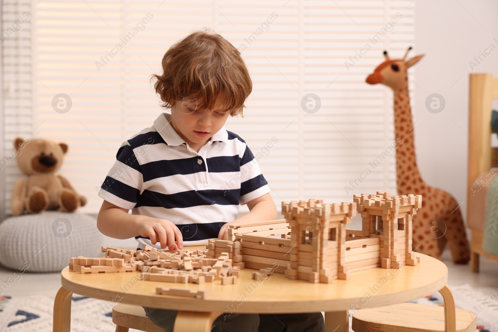 Photo of Cute little boy playing with wooden construction set at table in room. Child's toy