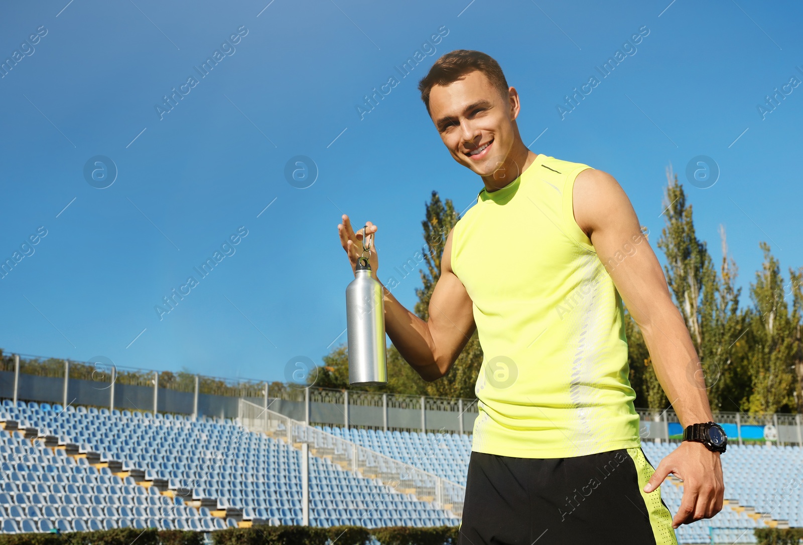 Photo of Sporty man with bottle of water at stadium on sunny day. Space for text