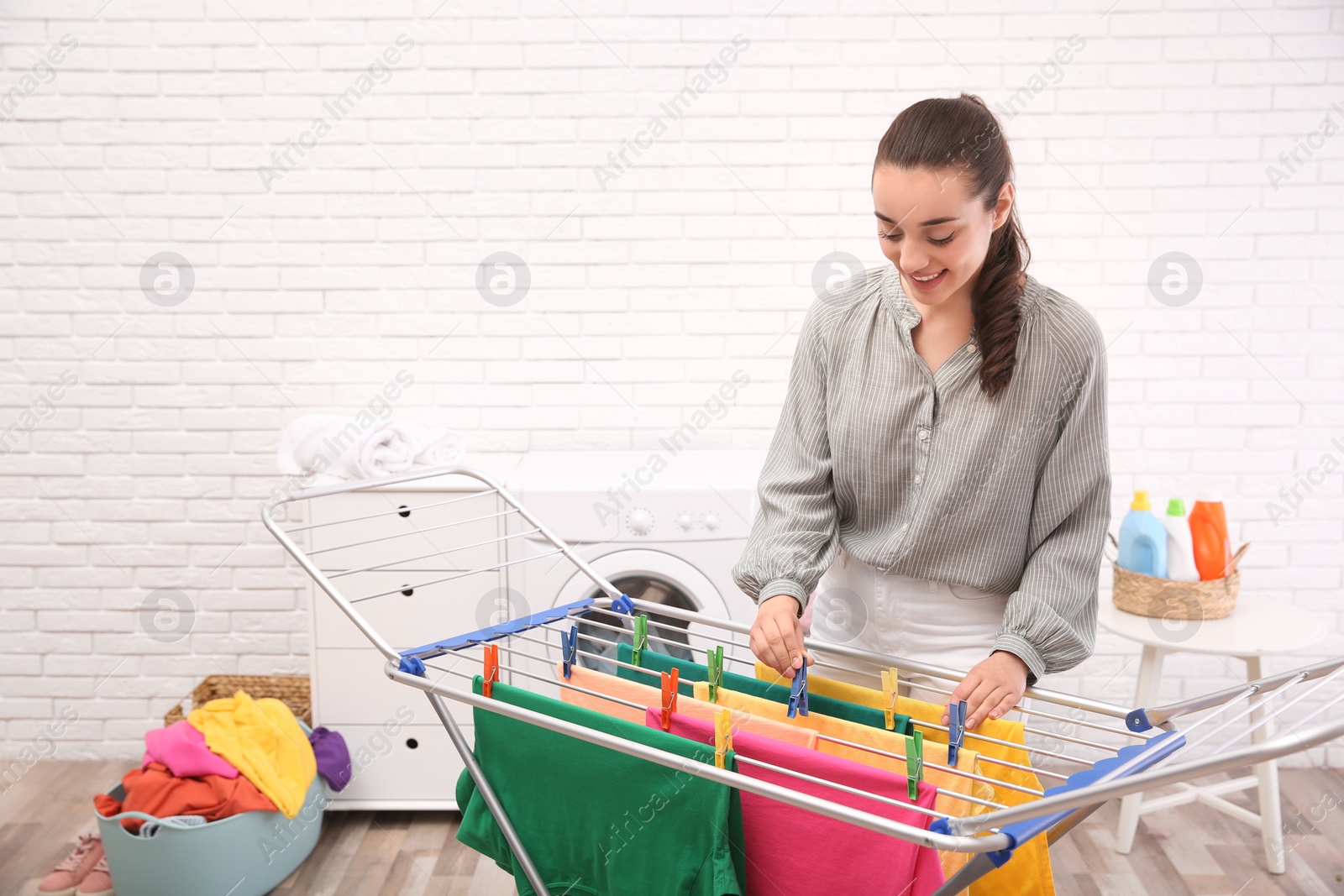 Photo of Young woman hanging clean laundry on drying rack indoors