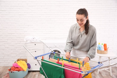 Photo of Young woman hanging clean laundry on drying rack indoors