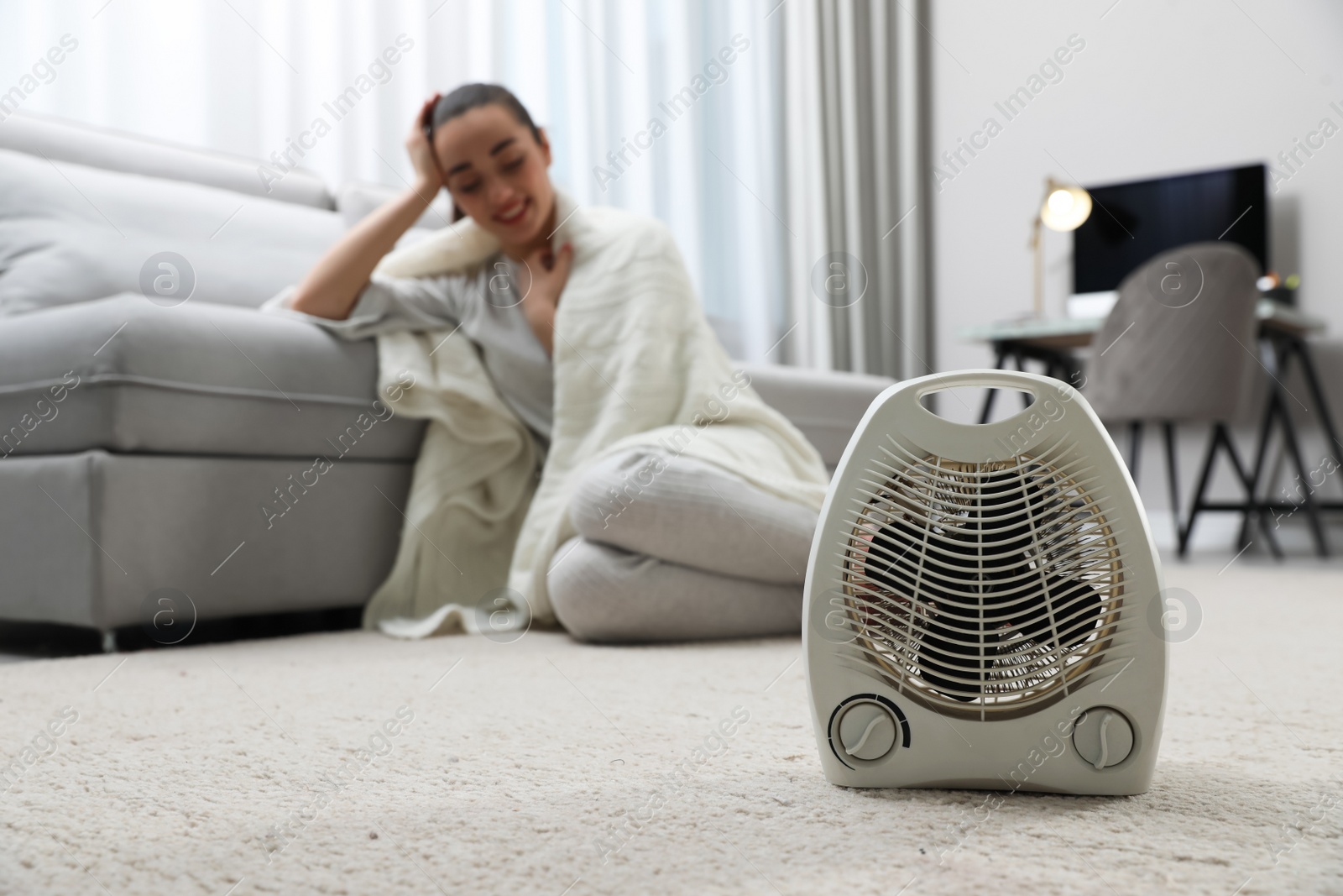 Photo of Electric heater and young woman with warm plaid indoors