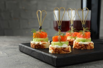 Photo of Tasty canapes with salmon, cucumber, bread and cream cheese served on grey table, closeup