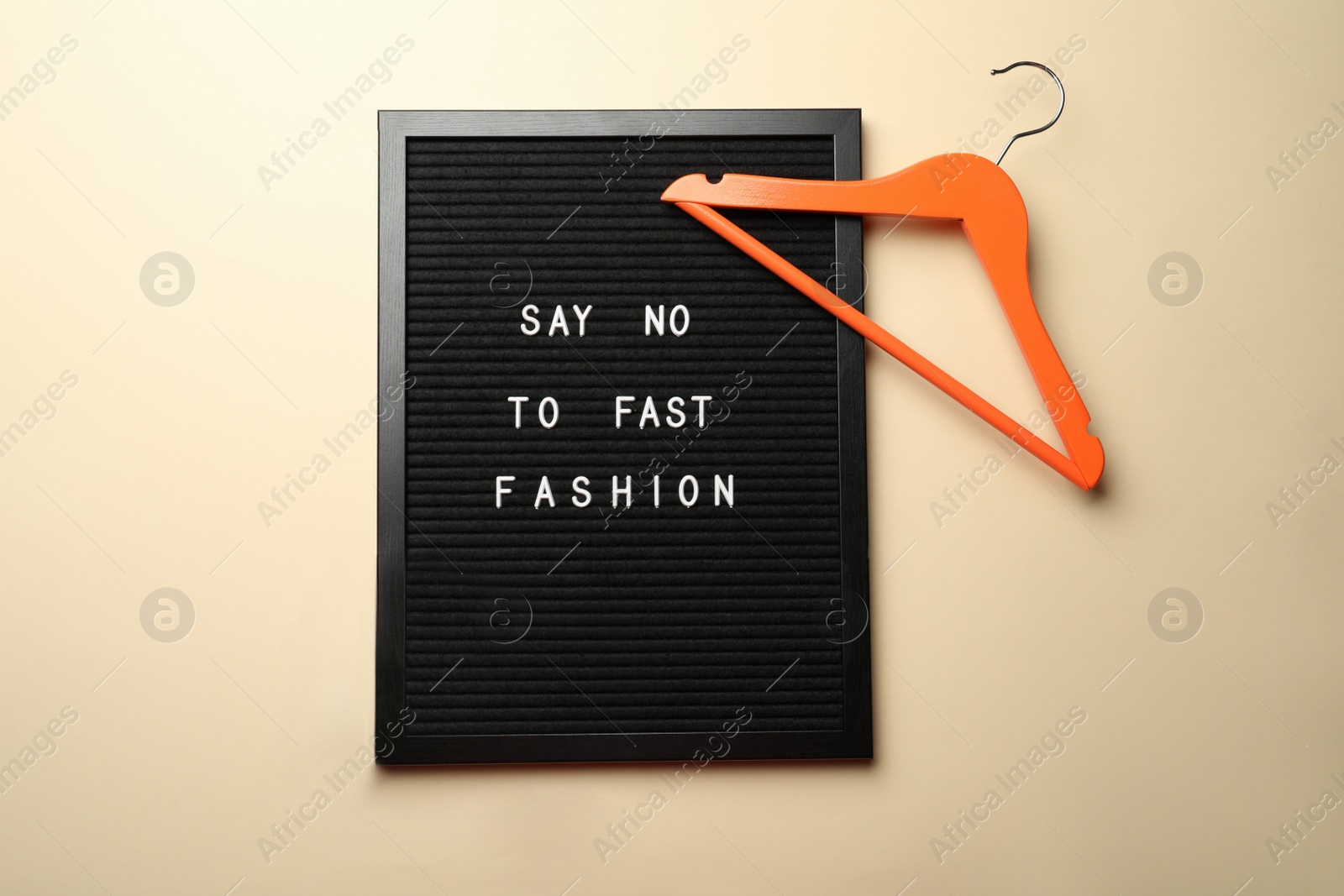 Photo of Black letter board with phrase SAY NO TO FAST FASHION, orange hanger on beige background, flat lay