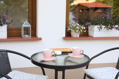 Photo of Cups of coffee, bread and cheese on glass table. Relaxing place at outdoor terrace
