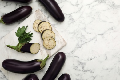 Photo of Cut and whole raw ripe eggplants on white marble table, flat lay. Space for text