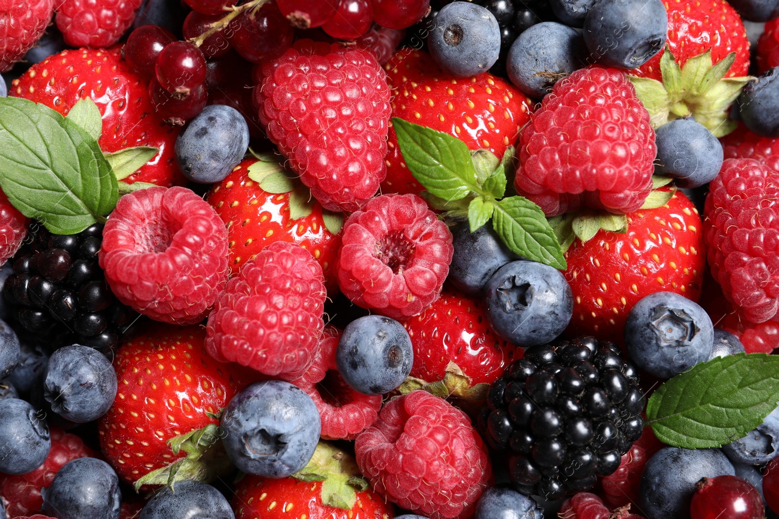 Photo of Assortment of fresh ripe berries with green leaves as background, top view