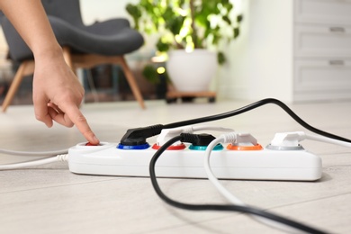 Woman pressing power button of extension cord on floor indoors, closeup. Electrician's professional equipment