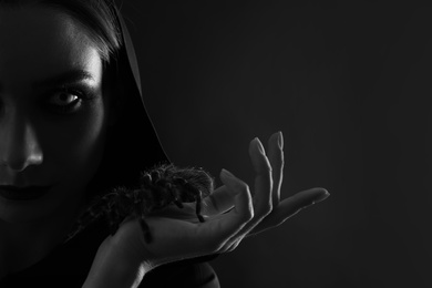 Photo of Mysterious witch with spooky spider on dark background, closeup. Black and white effect