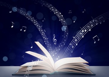 Image of Music flowing from book. Musical symbols flying over tome on grey table against dark blue background