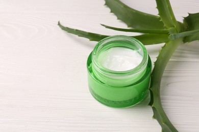 Photo of Jar of cosmetic cream and aloe vera leaves on white wooden table, closeup. Space for text