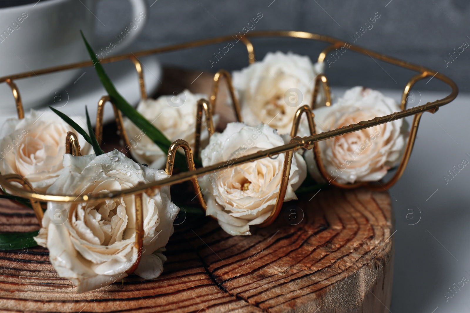 Photo of Decorative gold holder with flowers on wooden stand, closeup. Interior design