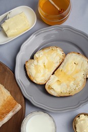 Photo of Sandwiches with butter, honey and milk on light grey table, flat lay