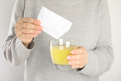 Woman pouring powder from medicine sachet into glass with water, closeup