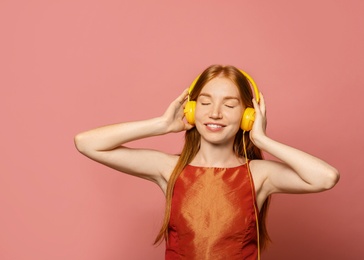 Portrait of beautiful young woman with headphones on pink background