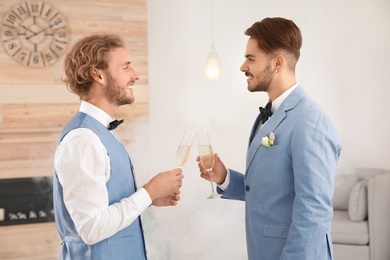 Happy newlywed gay couple with glasses of champagne at home