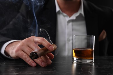 Photo of Man with glass of whiskey smoking cigar at dark marble table, closeup